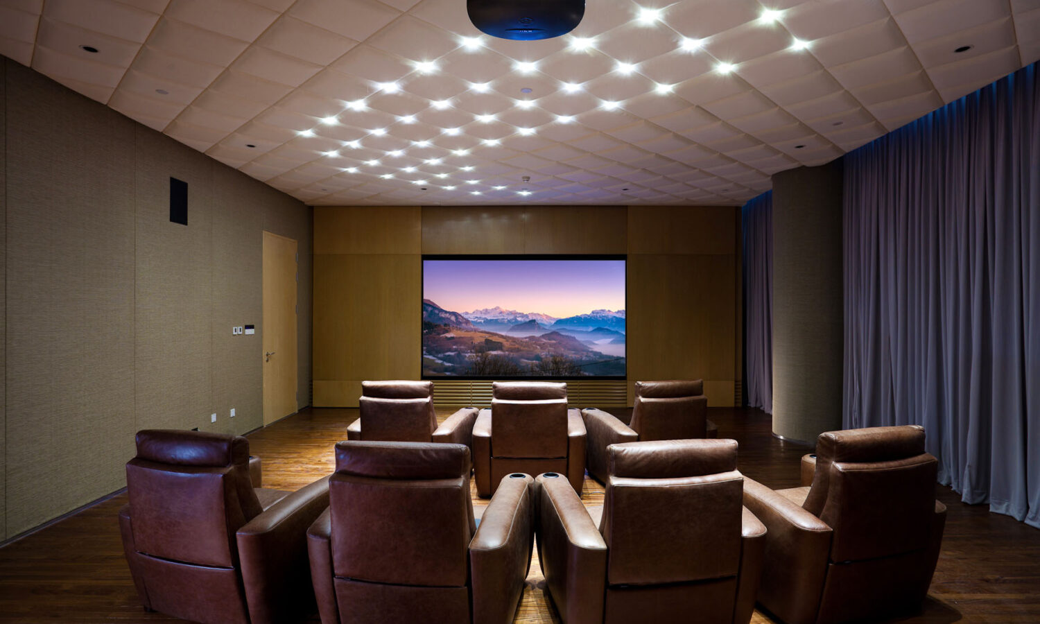 Modern home theater with two rows of brown leather recliners facing a large screen showing a mountain landscape.