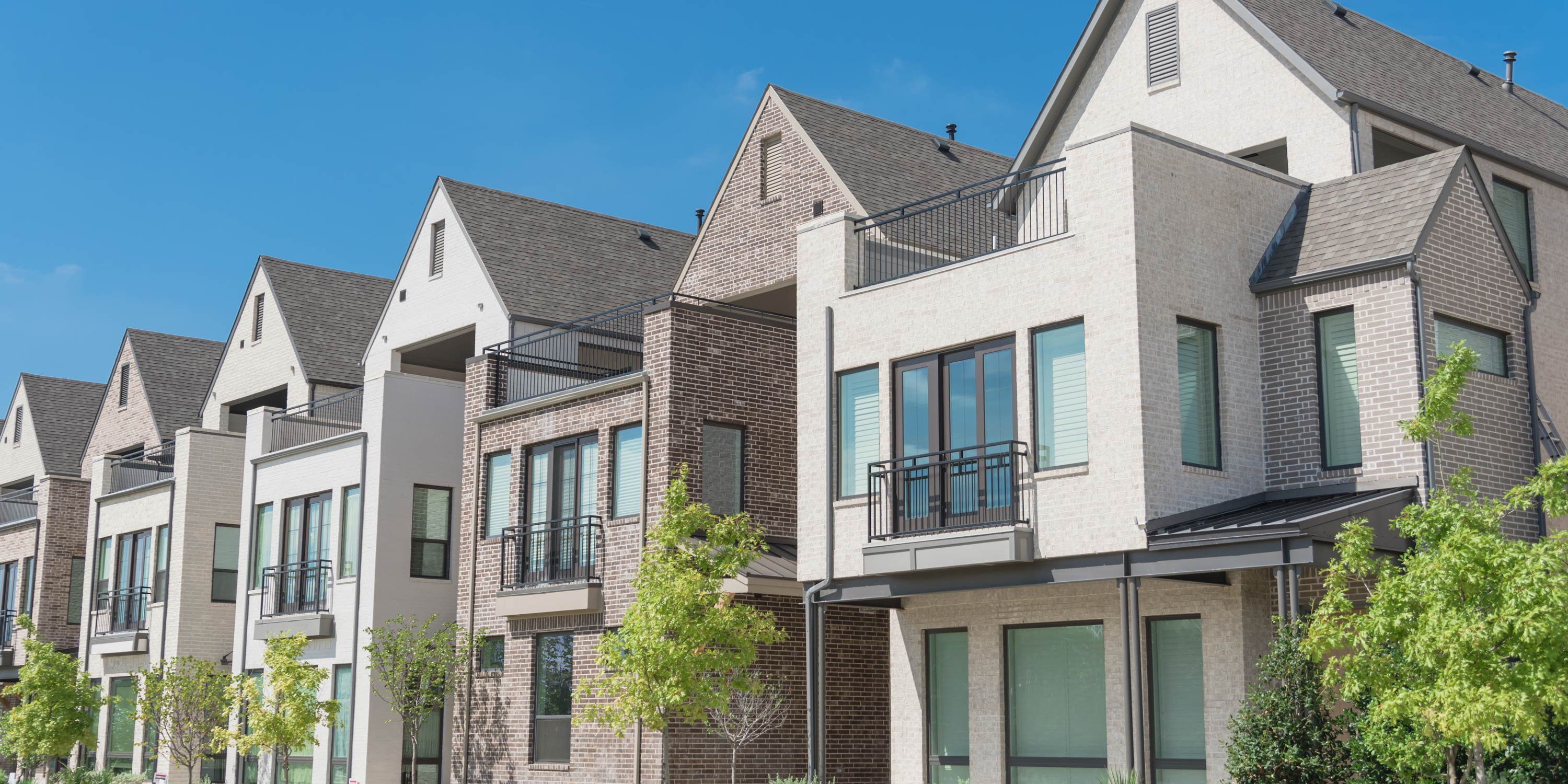 Row of modern multi-story townhomes with balconies and gabled roofs