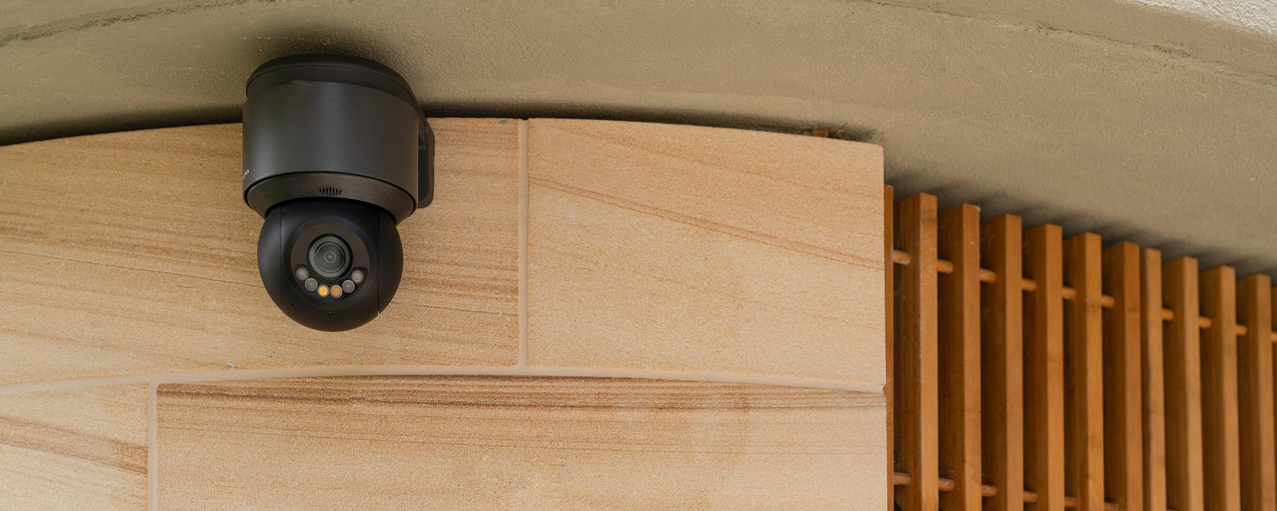 Outdoor security camera mounted under a roof edge with wooden slat siding