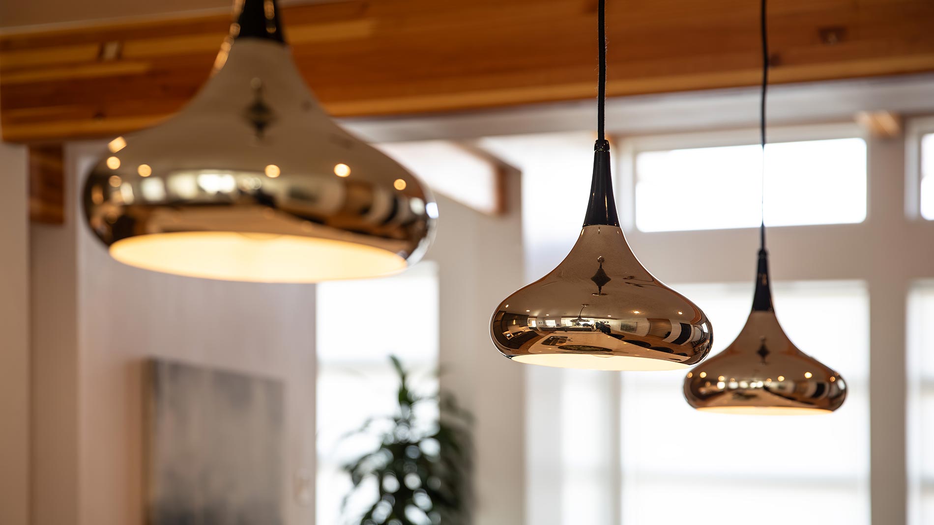 Trio of modern brass pendant lights hanging in a well-lit room with wood accents