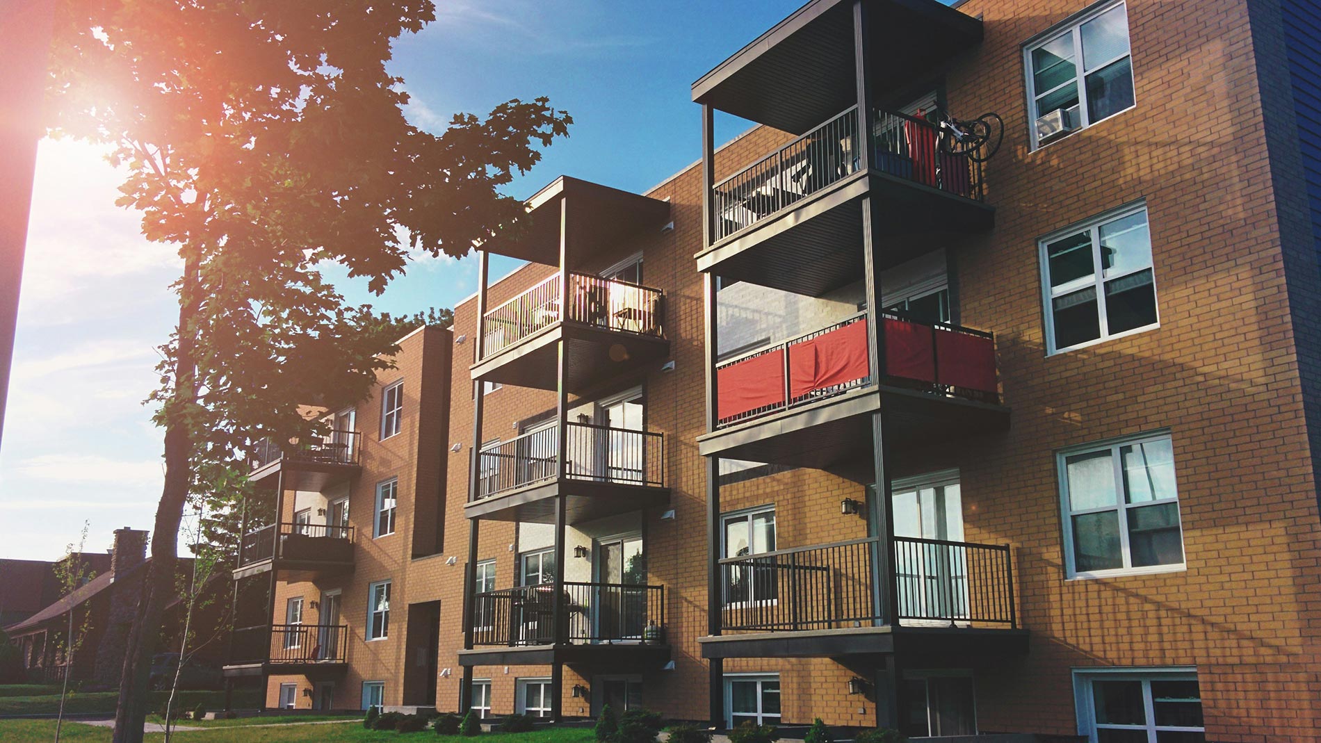 Sunlit apartment building with balconies and red fabric shades on upper levels