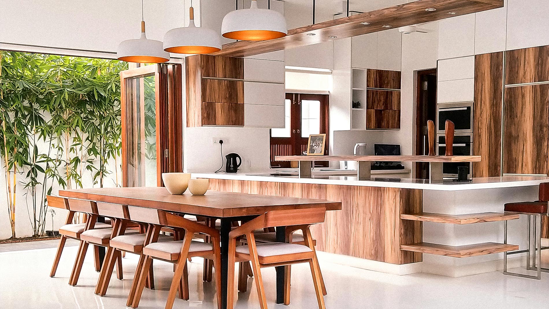 Bright contemporary kitchen with wooden finishes, large dining table, and pendant lights