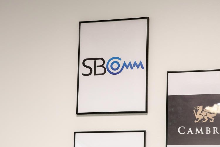 Framed SBComm logo sign mounted on an office wall