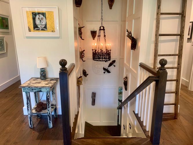 Top of staircase with dark wood railing, hanging chandelier, and wall masks