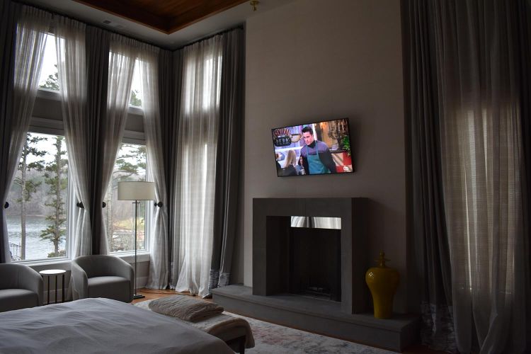 Bedroom with tall windows, sheer curtains, and TV above a modern fireplace