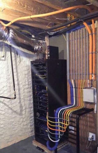 Organized home server rack with color-coded cables and exposed ceiling pipes
