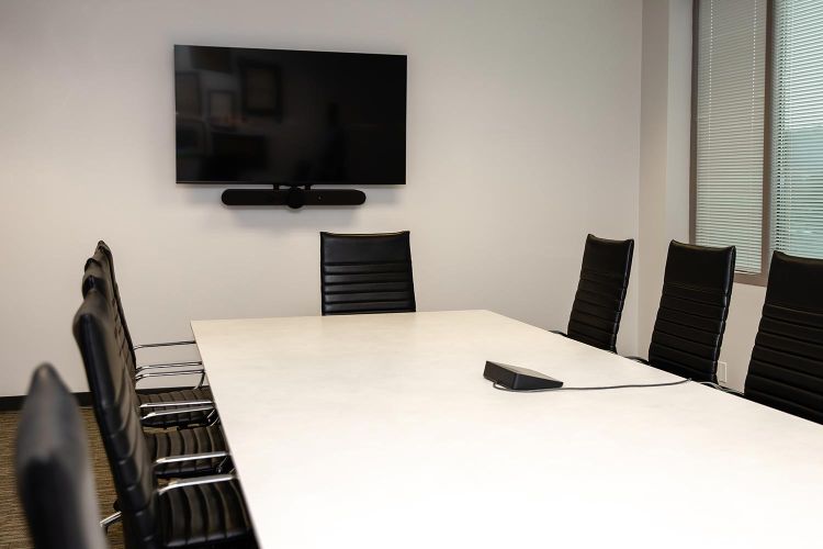 Conference room with table, chairs, wall-mounted TV, and video bar setup