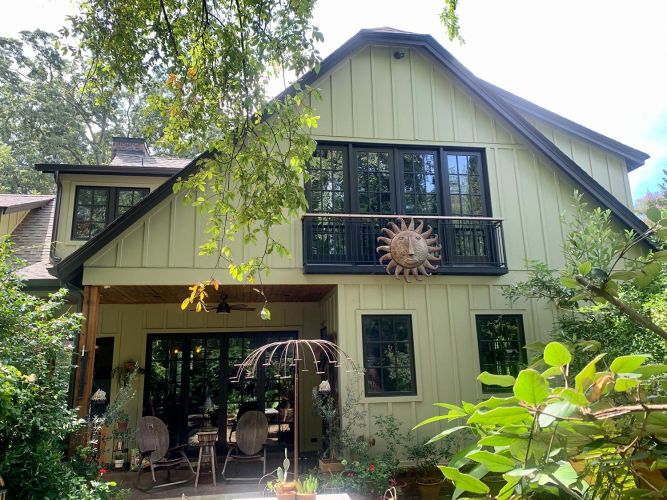 Green exterior of house with upper balcony, sun-face decor, and patio below
