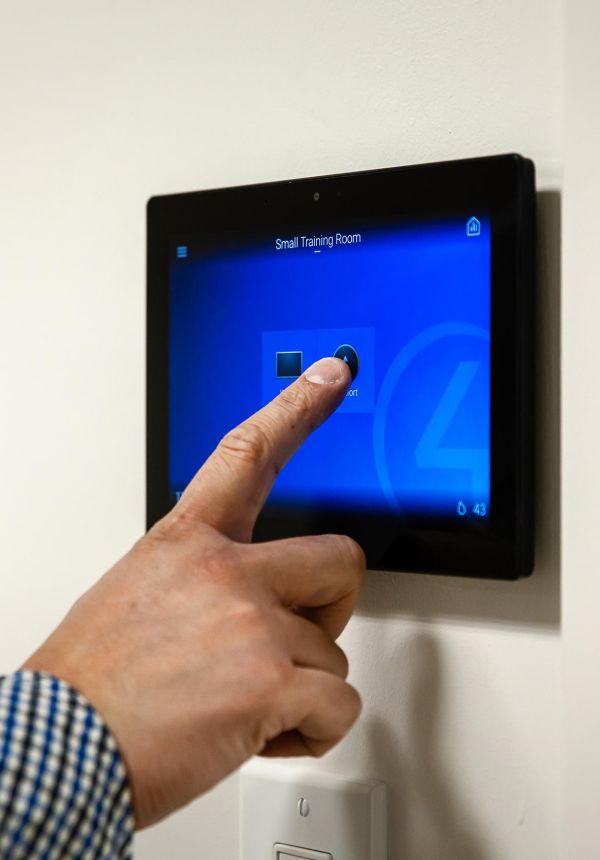 Hand pressing touchscreen wall panel labeled &ldquo;Small Training Room&rdquo;