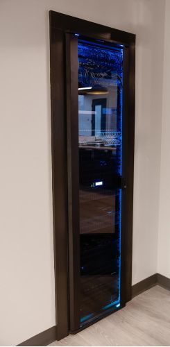 Tall black server rack with glowing blue lights enclosed behind a glass door