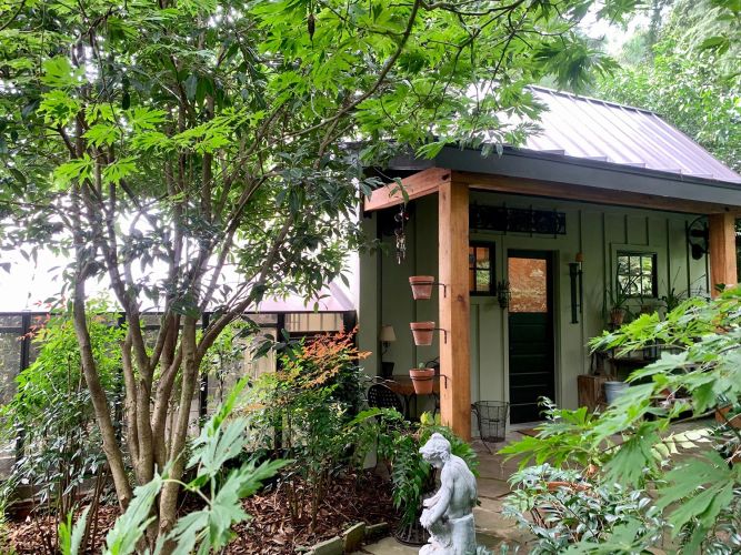 Covered porch with rocking chairs, lush greenery, and lined watering cans