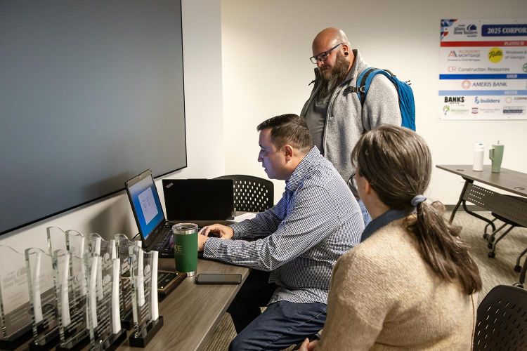 Man using a laptop in a conference room while two people watch