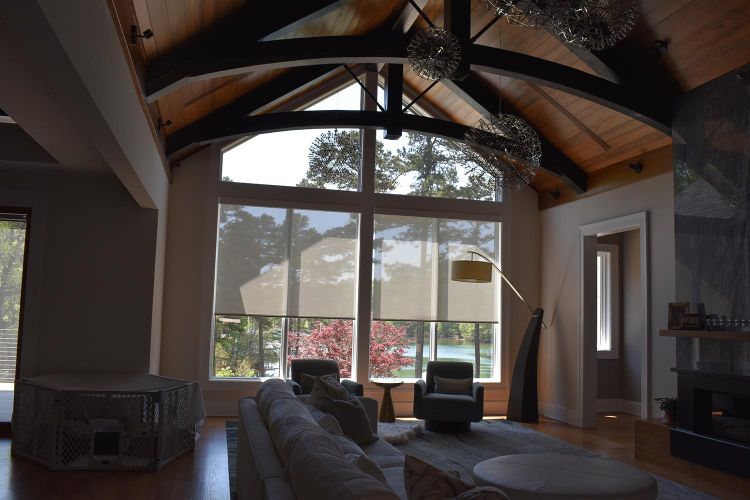 Living room with vaulted ceiling, massive windows, and two lounge chairs facing lake view