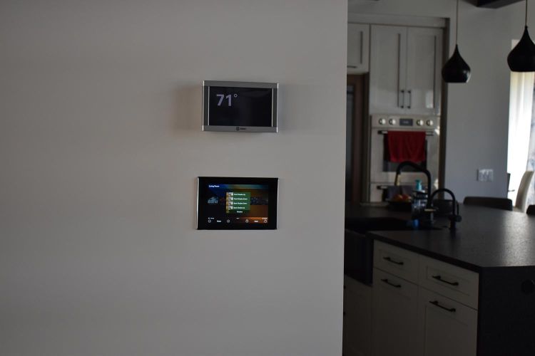 Wall-mounted thermostat and touchscreen control panel near a dark kitchen island