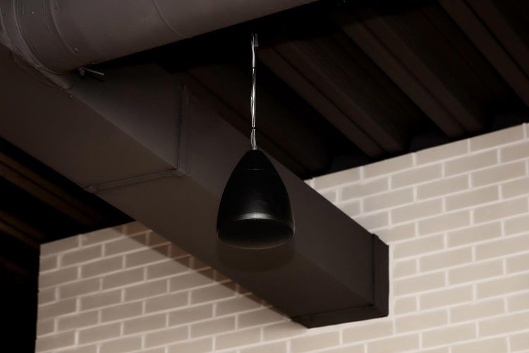 Ceiling-mounted pendant speaker against exposed duct and brick wall