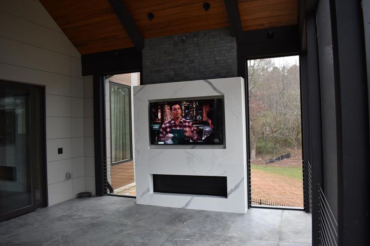 Covered patio area with mounted TV and marble surround, surrounded by trees