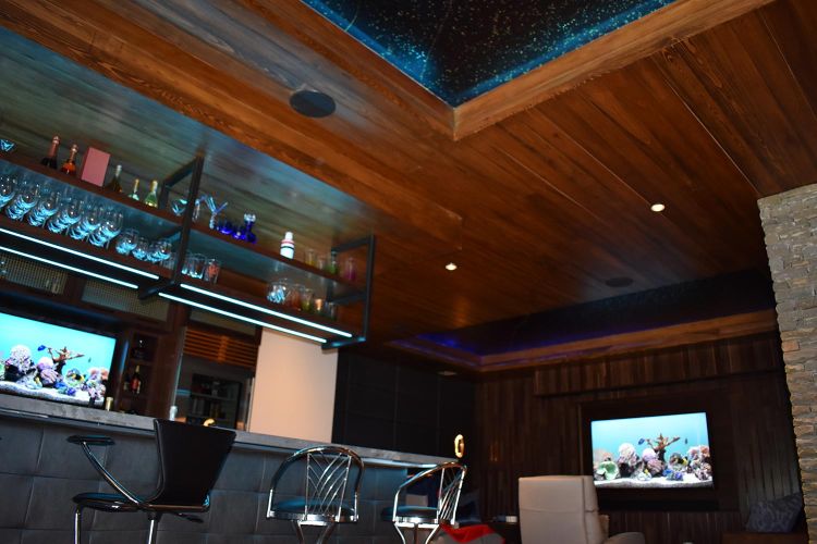 Home bar with hanging glass shelves, leather bar stools, and a ceiling aquarium panel