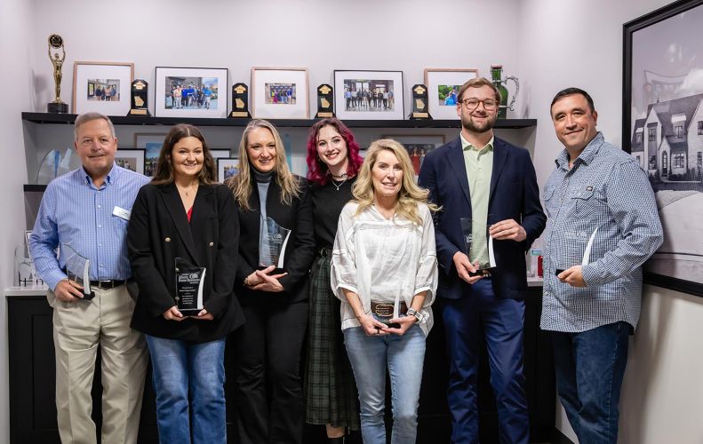 Group of award recipients posing with trophies in front of framed photos