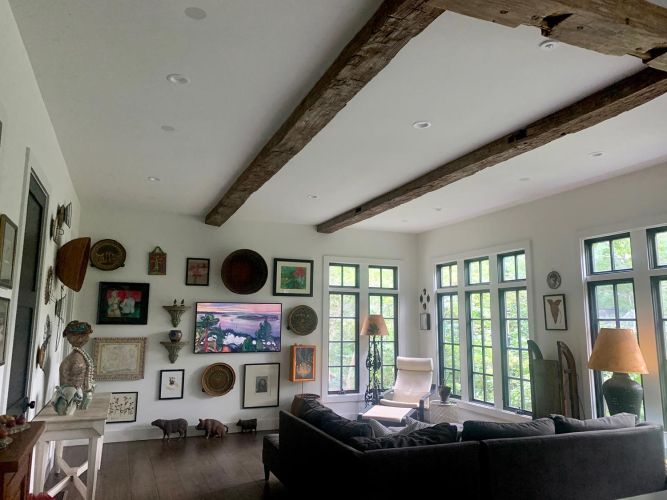 Bright living room with large windows, rustic beams, and a gallery wall above a TV