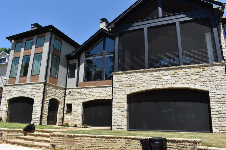 Modern lakefront home with stone and wood exterior, large screened porches, and arched patio openings