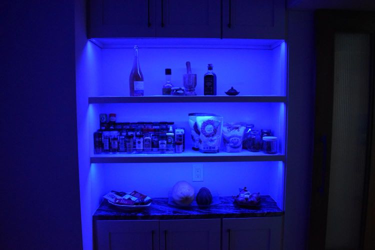 Illuminated pantry shelves in blue light showcasing spices, snacks, and bottles