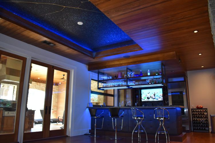 Modern home bar with blue lighting, hanging shelves, and bar stools