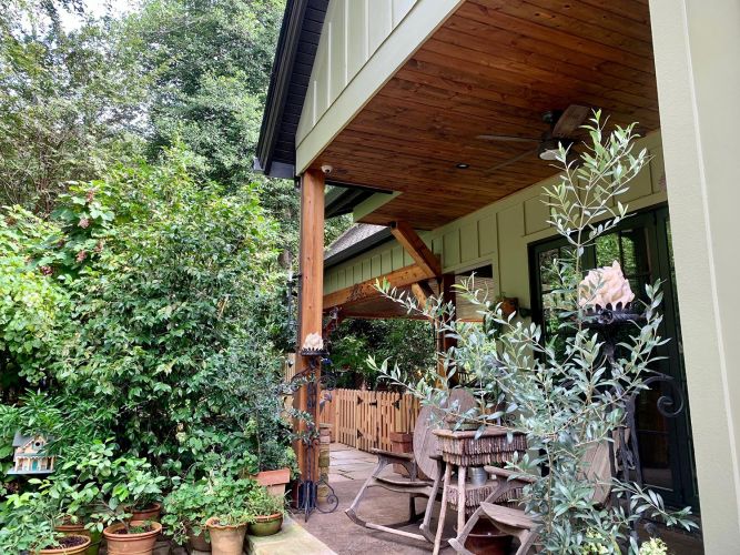 Covered patio with rocking chairs and potted plants beside lush greenery