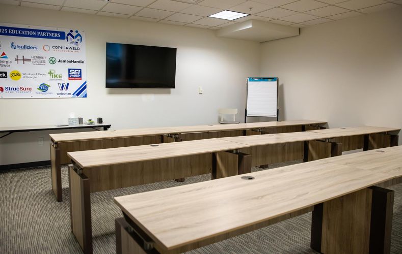 Empty classroom-style training room with wooden desks and a TV screen on the wall