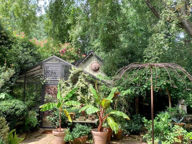 Lush garden view with greenhouse, banana plants, and metal arbor structure