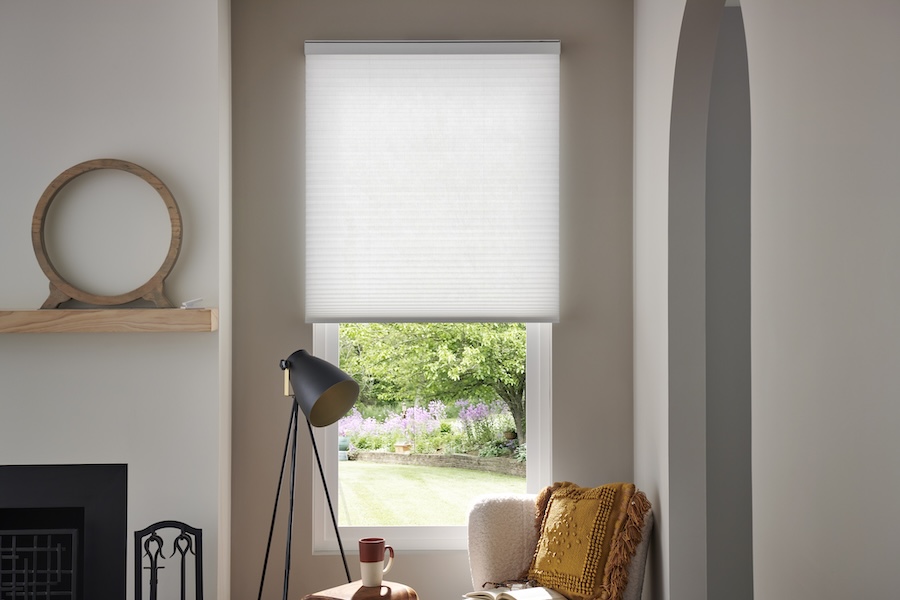 Motorized shades are partially open near a chair and lamp.